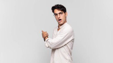 Genç yakışıklı adam şaşkın ve şaşırmış hissediyor. Kenardaki fotokopi alanını işaret ediyor. Şaşırmış, ağzı açık bir bakış.