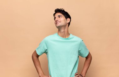 Genç yakışıklı adam mutlu, neşeli ve kendinden emin görünüyor. Gururla gülümsüyor ve iki elini de kalçasında istiyor.