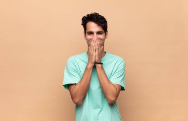 Genç yakışıklı adam mutlu, neşeli, şanslı ve şaşkın görünüyor. İki eliyle ağzını kapatıyor.