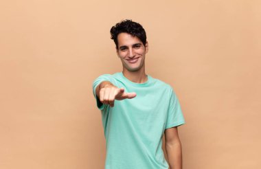 Genç ve yakışıklı bir adam kameraya bakıyor. Tatmin olmuş, kendine güvenen, dost canlısı bir gülümsemeyle seni seçiyor.