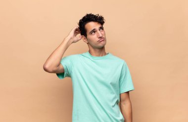 Genç yakışıklı adam şaşkın ve şaşkın hissediyor, başını kaşıyor ve yana bakıyor.