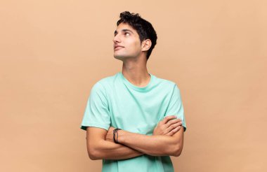 Genç yakışıklı adam mutlu, gururlu ve umutlu, merak ediyor ya da düşünüyor, çapraz kollarla boşluğu dolduruyor.