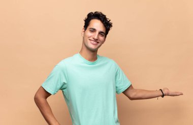 Genç yakışıklı adam kendini mutlu ve neşeli hissediyor, gülümsüyor ve seni selamlıyor, dostça bir jestle içeri davet ediyor.