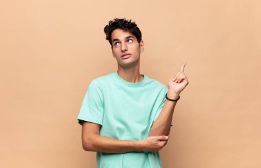 Genç yakışıklı adam mutlu bir şekilde gülümsüyor ve yan bakıyor, merak ediyor, düşünüyor ya da bir fikri var.