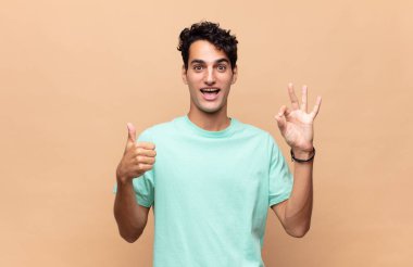 Genç yakışıklı adam kendini mutlu, şaşkın, tatmin olmuş ve şaşırmış hissediyor, tamam gösteriyor ve el kol hareketleri yapıyor, gülümsüyor.