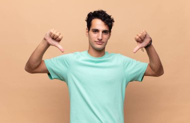 Genç yakışıklı adam üzgün, hayal kırıklığına uğramış ya da kızgın görünüyor, anlaşmazlık içinde baş parmağını gösteriyor, hayal kırıklığına uğramış hissediyor.