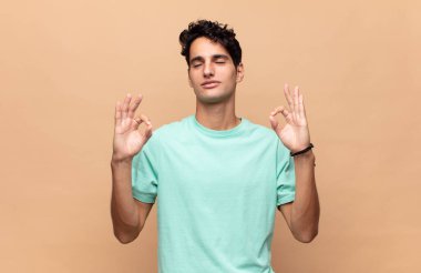 Genç yakışıklı adam konsantre olmuş ve meditasyon yapıyor, kendini tatmin olmuş ve rahatlamış hissediyor, düşünüyor ya da bir seçim yapıyor.