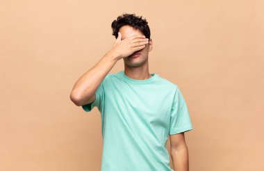 Genç yakışıklı bir adam tek eliyle gözlerini kapatıyor. Korkmuş ya da endişeli, merak ediyor ya da körü körüne bir sürpriz bekliyor.