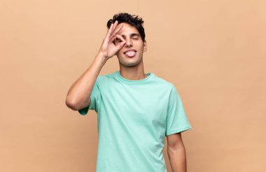 Genç yakışıklı adam mutlu bir şekilde gülümsüyor, şaka yapıyor ve gözetleme deliğinden bakıyor, sırları gözetliyor.