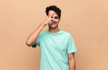 Genç yakışıklı adam şok olmuş, korkmuş ya da korkmuş görünüyor. Yüzü elle kaplanmış ve parmaklarının arasından gizlice bakıyor.