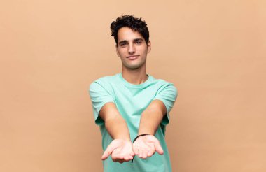 Genç yakışıklı adam mutlu bir şekilde gülümsüyor arkadaş canlısı, kendinden emin, olumlu bakışlı, bir nesne ya da konsept sunuyor ve gösteriyor.