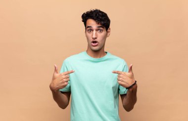 Genç yakışıklı adam mutlu, şaşkın ve gururlu, heyecanlı, şaşkın bakışlarıyla kendini işaret ediyor.