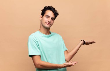 Genç yakışıklı adam gururla ve kendinden emin bir şekilde gülümsüyor, mutlu ve tatmin olmuş hissediyor ve fotokopi alanında bir konsept gösteriyor.