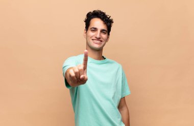 Genç ve yakışıklı bir adam gururla gülümsüyor ve gururla bir numaralı pozu veriyor, kendini lider gibi hissediyor.