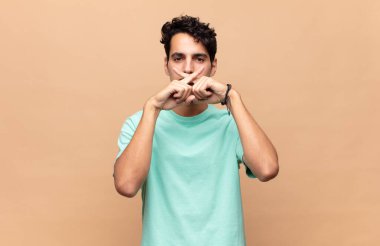 Genç ve yakışıklı bir adam ciddi ve hoşnutsuz görünüyor. İki parmağın önde olsun, reddedilsin ve sessizlik istesin.