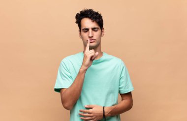 Genç ve yakışıklı adam ciddi görünüyor ve parmaklarını dudaklarına bastırıp sessizlik ya da sessizlik talep ediyor, sır saklıyor.