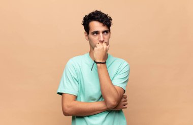 Genç yakışıklı adam ciddi, düşünceli ve endişeli, elleri çenesine bastırılmış, yan bakıyor.