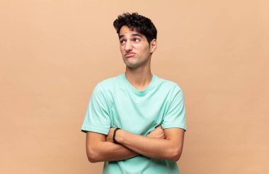 Genç yakışıklı adam omuz silkiyor, kafası karışık ve kararsız, kolları bağlı ve şaşkın görünüyor.