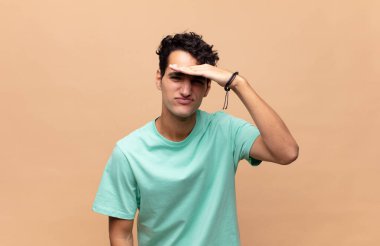 Genç yakışıklı adam şaşkın ve şaşkın bakıyor, el üstünde uzak bakıyor, izliyor ya da arıyor