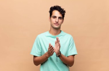 Genç yakışıklı adam kendini mutlu ve başarılı hissediyor, gülümsüyor ve alkışlıyor, alkışlarla tebrik ediyor.