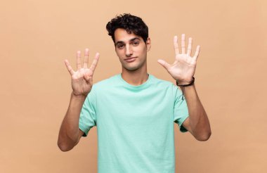 Genç yakışıklı adam gülümsüyor ve arkadaş canlısı görünüyor. 9 ya da 9 numarayı gösteriyor. Elleri önde, geriye doğru sayıyor.