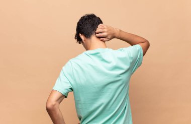 Genç yakışıklı adam düşünüyor ya da şüphe ediyor, kafasını kaşıyor, şaşkın ve kafası karışık hissediyor, arkaya ya da arkaya bakıyor.