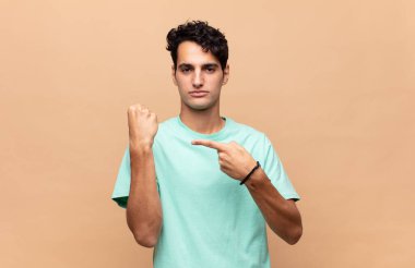 Genç yakışıklı adam sabırsız ve kızgın görünüyor, saati gösteriyor, dakiklik istiyor, zamanında gelmek istiyor.