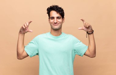 Genç yakışıklı bir adam kendi gülüşünü çiziyor ya da özetliyor iki eliyle, pozitif ve mutlu görünüyor, sağIık kavramı.