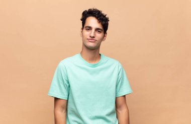 Genç yakışıklı adam pozitif ve kendinden emin gülümsüyor. Tatmin olmuş, arkadaş canlısı ve mutlu görünüyor.