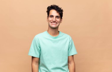 Genç yakışıklı adam mutlu ve şapşal görünüyor. Geniş, eğlenceli, kaçık bir gülüşü ve açık gözleri var.