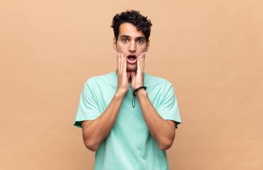 Genç yakışıklı adam şok olmuş ve korkmuş hissediyor, ağzı açık ve elleri yanaklarında korkmuş görünüyor.