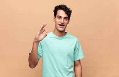 Genç yakışıklı adam kendini başarılı ve tatmin olmuş hissediyor, ağzı açık gülümsüyor, elle işaret veriyor.
