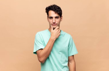 Genç yakışıklı adam ciddi görünüyor, kafası karışık, kararsız ve düşünceli, seçenekler ve seçimler arasında şüpheci.