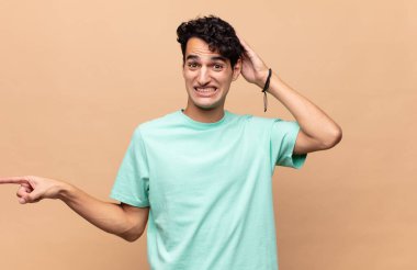 Genç yakışıklı adam gülüyor, mutlu, pozitif ve şaşırmış görünüyor. Yan fotokopi alanını işaret eden harika bir fikrin farkına varıyor.