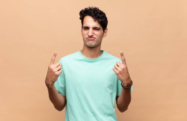 Kötü tavırlı genç yakışıklı adam gururlu ve agresif görünüyor, yukarıyı işaret ediyor ya da elleriyle alay işareti yapıyor.