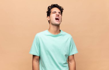Genç yakışıklı adam öfkeyle bağırıyor, agresif bir şekilde bağırıyor, stresli ve sinirli görünüyor.