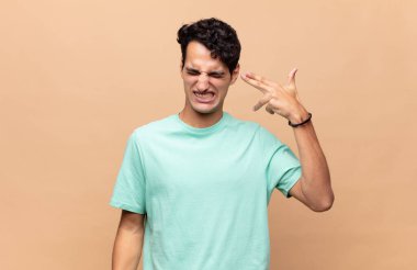 Genç yakışıklı adam mutsuz ve stresli görünüyor, intihar jesti silahla işaret ediyor, kafasını işaret ediyor.