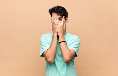 Genç ve yakışıklı bir adam korkmuş ya da utanmış hissediyor. Gözleri yarı kapalı ya da ellerle dikizliyor ya da dikizliyor.