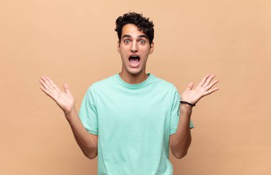 Genç yakışıklı adam mutlu ve heyecanlı görünüyor. Beklenmedik bir sürprizle şoke olmuş. İki eli yüzü açık.