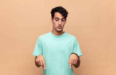 İki eliyle aşağıya bakan ağzı açık genç yakışıklı adam, şaşkın, şaşkın ve şaşırmış görünüyor.