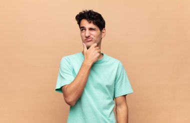 Genç yakışıklı adam düşünüyor, kuşkulu ve şaşkın hissediyor, farklı seçeneklerle, hangi kararı vereceğini merak ediyor.