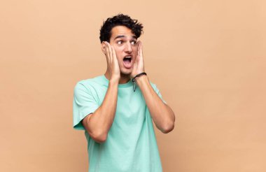 Genç yakışıklı adam mutlu, heyecanlı ve şaşırmış hissediyor, iki eli yüzü yana bakıyor.