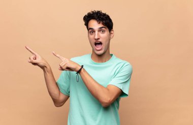 Genç, yakışıklı bir adam kendini neşeli ve şaşırmış hissediyor. Şok olmuş bir ifadeyle gülümsüyor ve bir tarafı işaret ediyor.