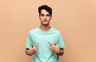 Genç ve yakışıklı bir adam kendini işaret ediyor. Şaşırmış ve şaşırmış bir şekilde bakıyor.