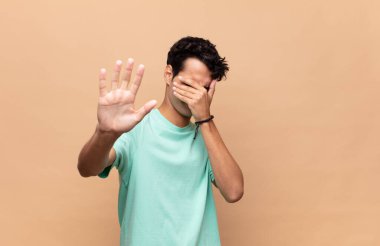 Genç ve yakışıklı bir adam elleriyle yüzünü kapatıyor ve kamerayı durdurmak için diğer elini öne koyuyor. Fotoğraf ya da resimleri reddediyor.