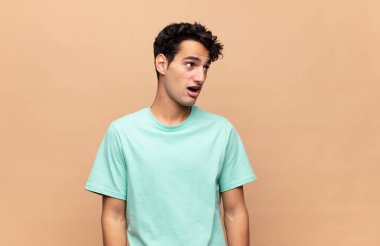 Genç yakışıklı adam şok olmuş, mutlu, şaşkın ve şaşırmış hissediyor, ağzı açık bir şekilde yana bakıyor.