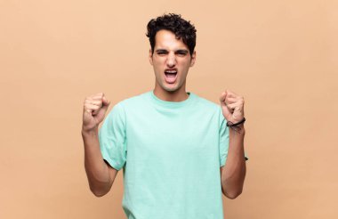 Genç yakışıklı bir adam sinirli bir ifadeyle ya da yumruklarıyla başarıyı kutlarken agresif bir şekilde bağırıyor.