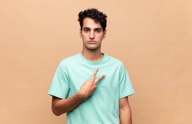 Genç yakışıklı adam kendini mutlu, pozitif ve başarılı hissediyor. Göğsünde el ile V şekli yapıyor. Zafer ya da huzur gösteriyor.