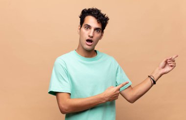 Genç yakışıklı adam şaşkın ve şaşırmış hissediyor. Kenardaki fotokopi alanını işaret ediyor. Şaşırmış, ağzı açık bir bakış.