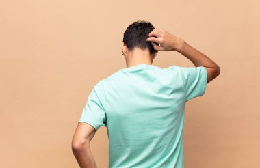 Genç yakışıklı bir adam bilgisiz ve kafası karışık hissediyor, bir çözüm düşünüyor, eli kalçasında, diğeri kafasında, dikiz aynasından.